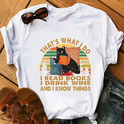 white t-shirt with a picture of a black cat leaning on a table top with book ijn hand and a glass of wine on the table, words on the t-shirt, That's what I do, I read books, I drink wine and I know things