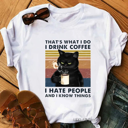 white t-shirt with a picture of a black cat about to take a drink of coffee, words on the t-shirt say, that's what I do I drink coffee, I hate people and I know things